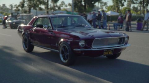 1993 Ford Taurus - Maroon 1969 Ford Mustang coupe with black racing stripes on hood, driving on asphalt.