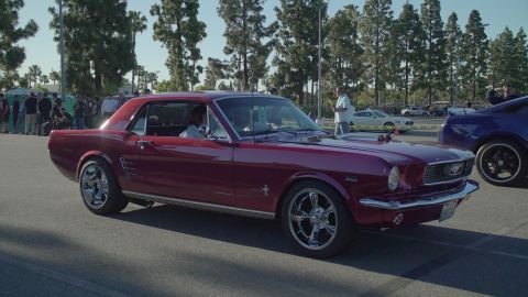 1993 Ford Taurus - A maroon 1965 Ford Mustang coupe is seen at an outdoor car show with other vehicles present.
