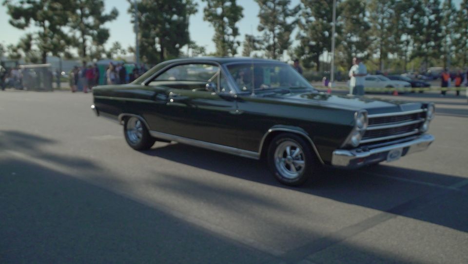 Dark green classic coupe driving on a paved road.
