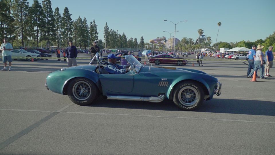 Teal blue classic convertible sports car with exposed exhaust pipes.