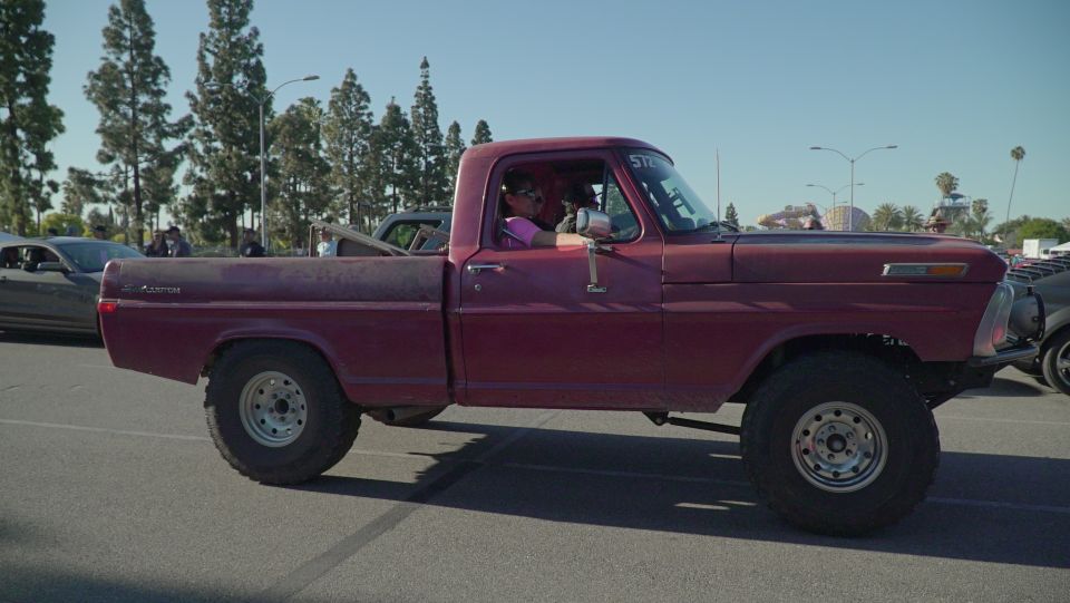Maroon lifted Ford F-Series pickup truck with off-road tires, driver visible.