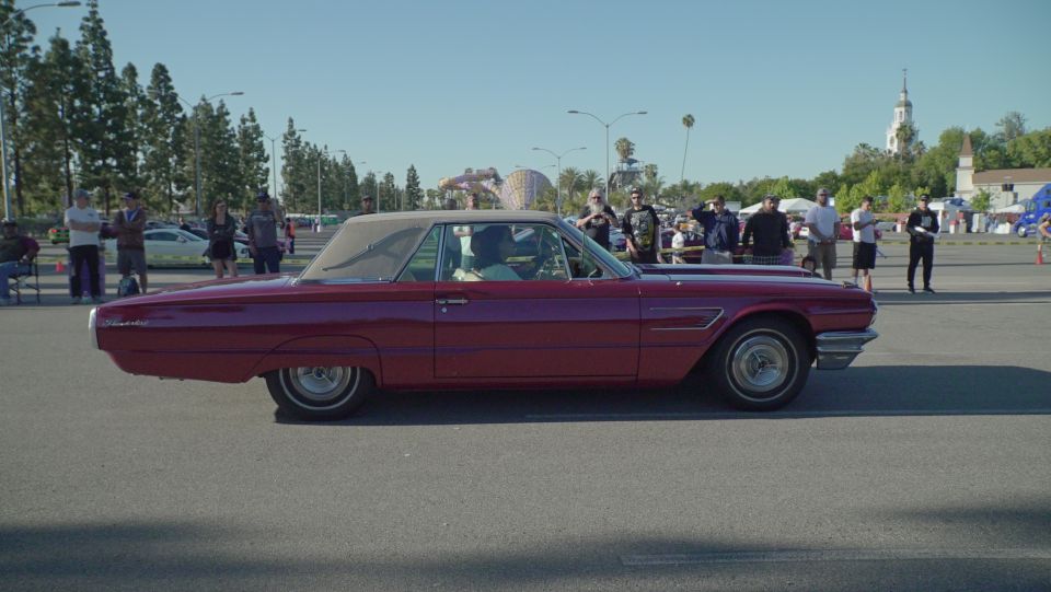 Red classic convertible Thunderbird parked in an asphalt lot with people in the background.