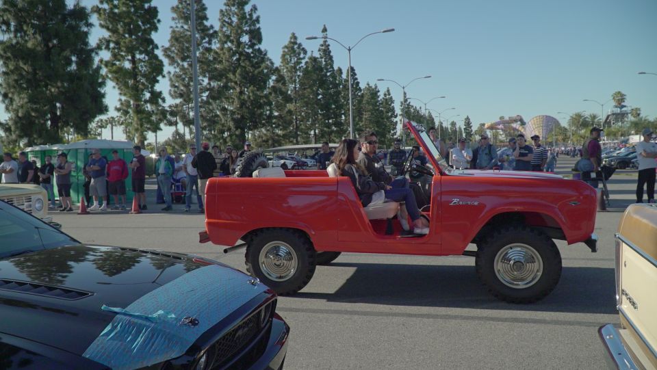 Red vintage Ford Bronco with people around it at an outdoor car show.