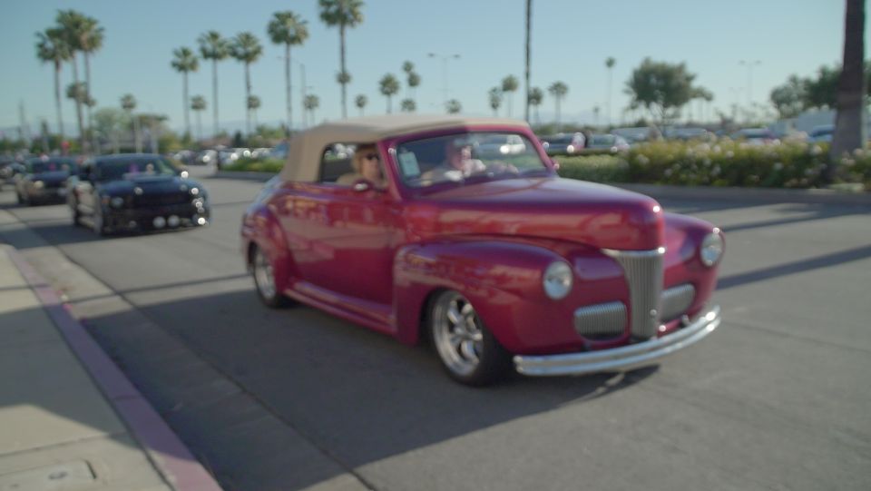 Red classic convertible car driving on a street with palm trees.