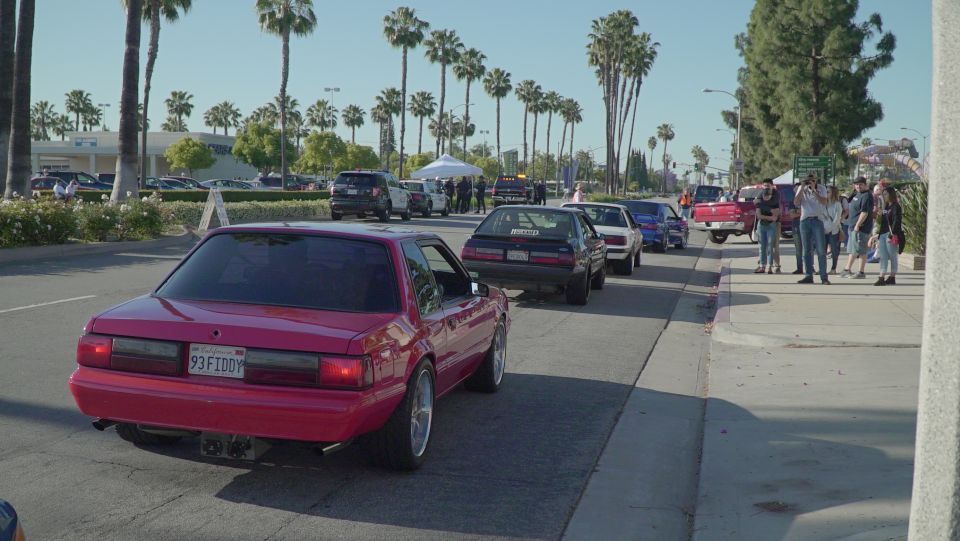Red 1993 Ford Mustang coupe with custom wheels and a license plate reading "93 FIDDY".