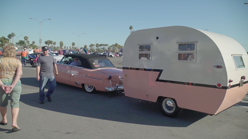Pink classic convertible car towing a vintage camper trailer