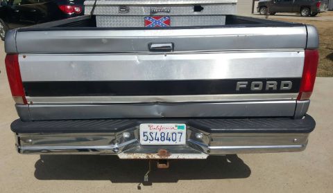 1995 Ford F-150 - The rear of a silver Ford pickup truck is shown, featuring a dented tailgate with the "FORD" logo and a California license plate reading "5…