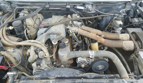 1995 Ford F-150 - A close-up, overhead view of a dirty, gray Ford V8 engine bay. Visible components include the intake manifold, hoses, belts, alternator, an…