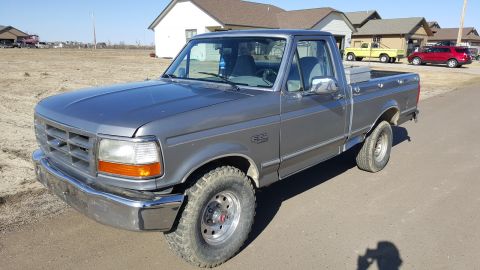 1995 Ford F-150 - A gray 1990s Ford F-150 pickup truck is parked on an asphalt road in front of a residential area. The truck is viewed from a 3/4 front angl…