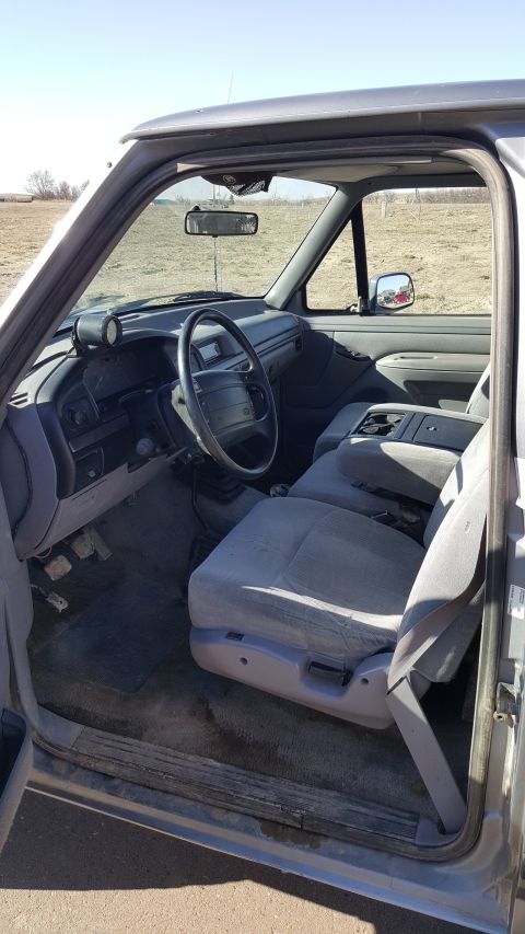 1995 Ford F-150 - The interior of a gray 1995 Ford F-150 is shown from the driver's side door. The image features the steering wheel, dashboard, center conso…