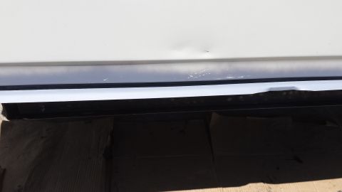 1976 Ford Ranchero - A close-up view of the lower body panel of a white vehicle, showing a dent and scratches on the dark trim below the main body.