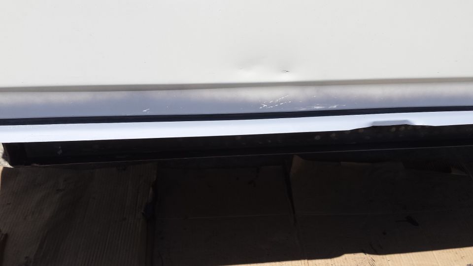 White vehicle lower body panel with dent and scratches on dark trim.