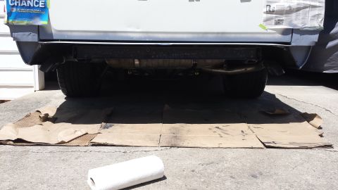 1976 Ford Ranchero - The rear underside of a vehicle is shown, with dual exhaust pipes visible. Cardboard is laid out on the ground beneath the vehicle, possibl…