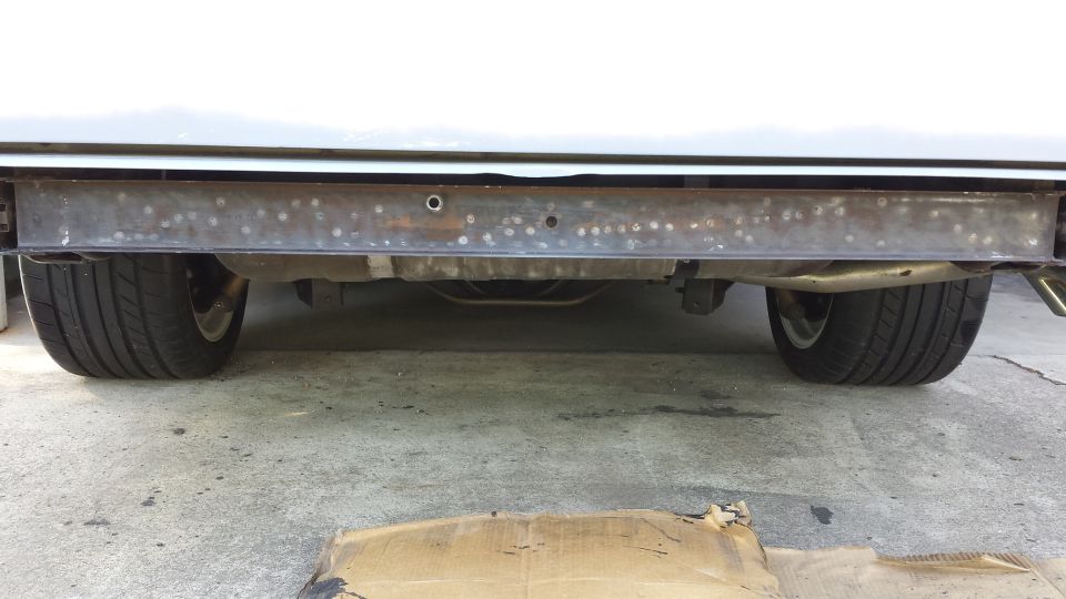 Underside of a vehicle showing rear bumper support, exhaust, and tires.