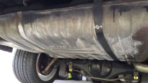 1976 Ford Ranchero - Undercarriage view of a vehicle, focusing on the fuel tank and rear differential. The fuel tank shows signs of wear and some dark staining.