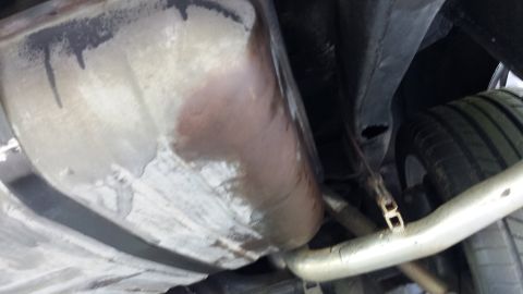 1976 Ford Ranchero - The underside of a vehicle shows a large, rusty fuel tank and part of the exhaust system. A tire is visible to the right, suggesting this i…
