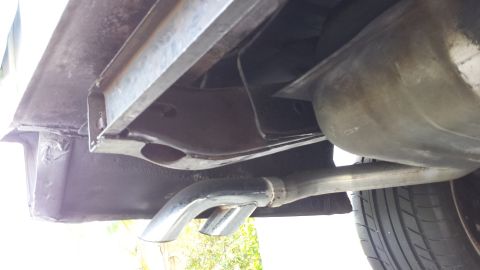 1976 Ford Ranchero - The underside of a vehicle shows a chrome exhaust tip exiting from the rear, with a portion of the fuel tank and chassis visible above it.…