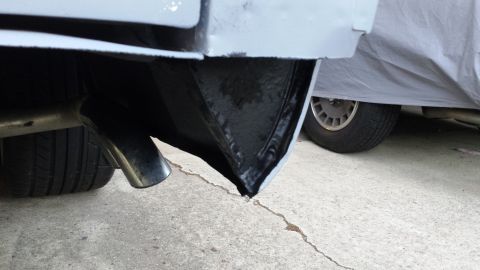 1976 Ford Ranchero - The underside of a vehicle's rear bumper and exhaust pipe are shown, with another vehicle partially covered by a tarp in the background.