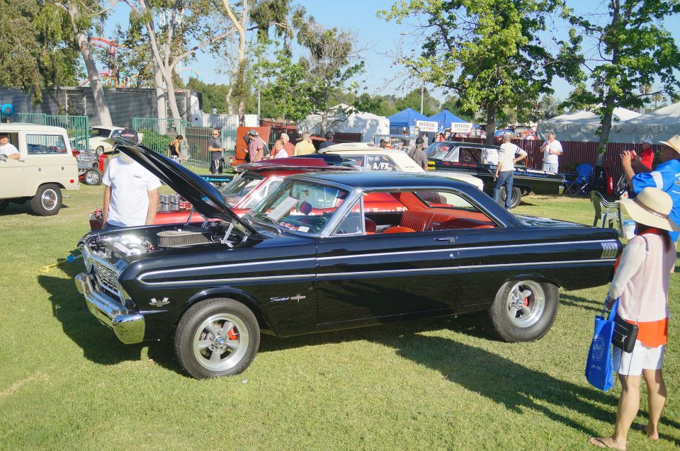 Black 1960s coupe with red interior at a car show, hood open.
