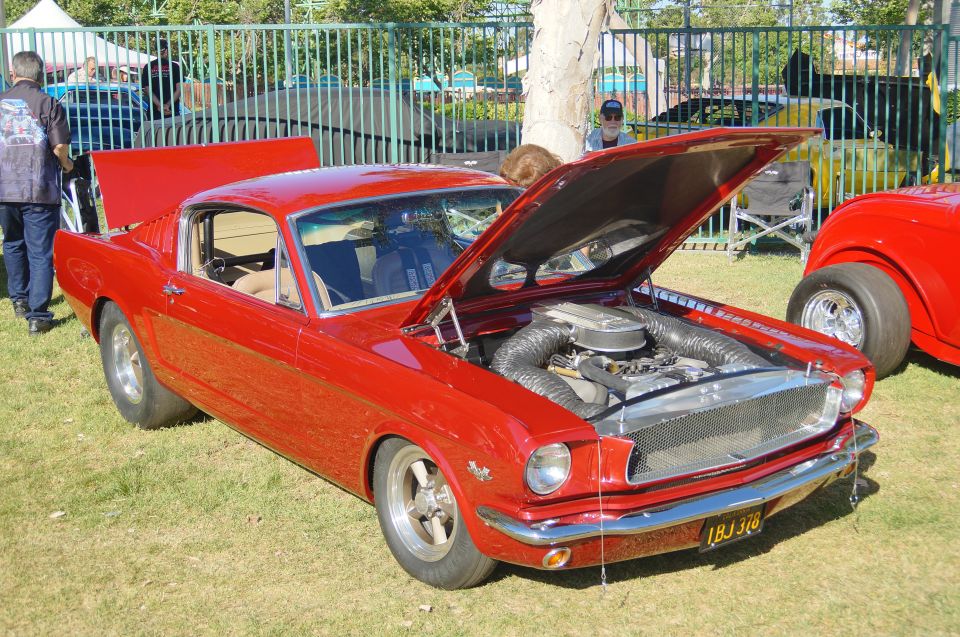 Red classic Ford Mustang with hood open, showing engine and intake.
