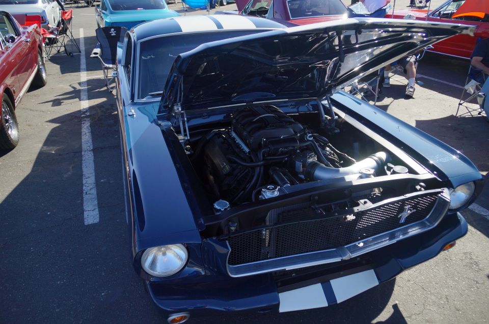 Dark blue classic Ford Mustang with hood open showing supercharged engine and white racing stripes.