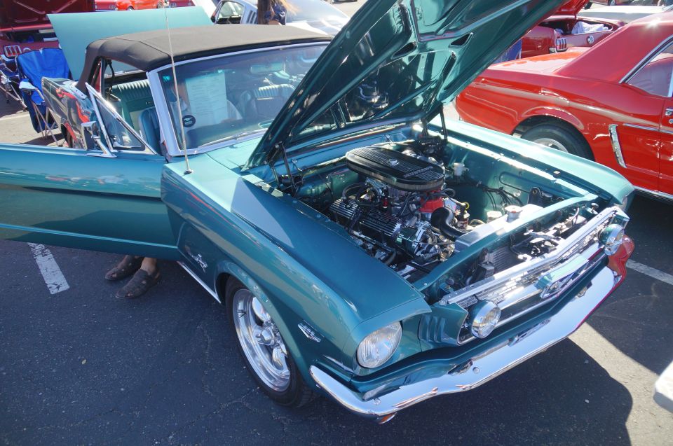 Teal classic convertible with hood open showing engine, parked next to a red classic car.
