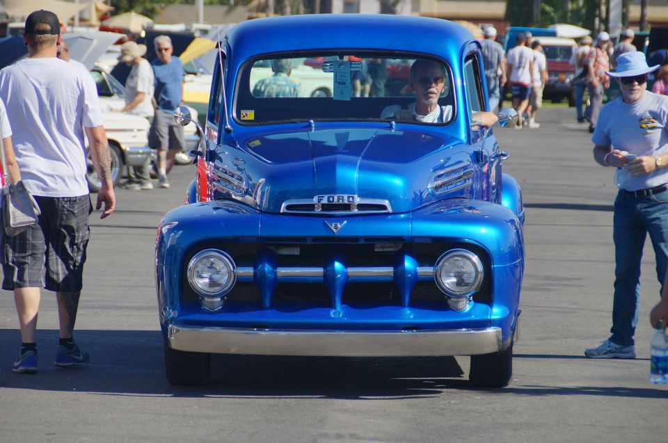 Blue Ford pickup truck with chrome grille and headlights, man in blue hat standing nearby.