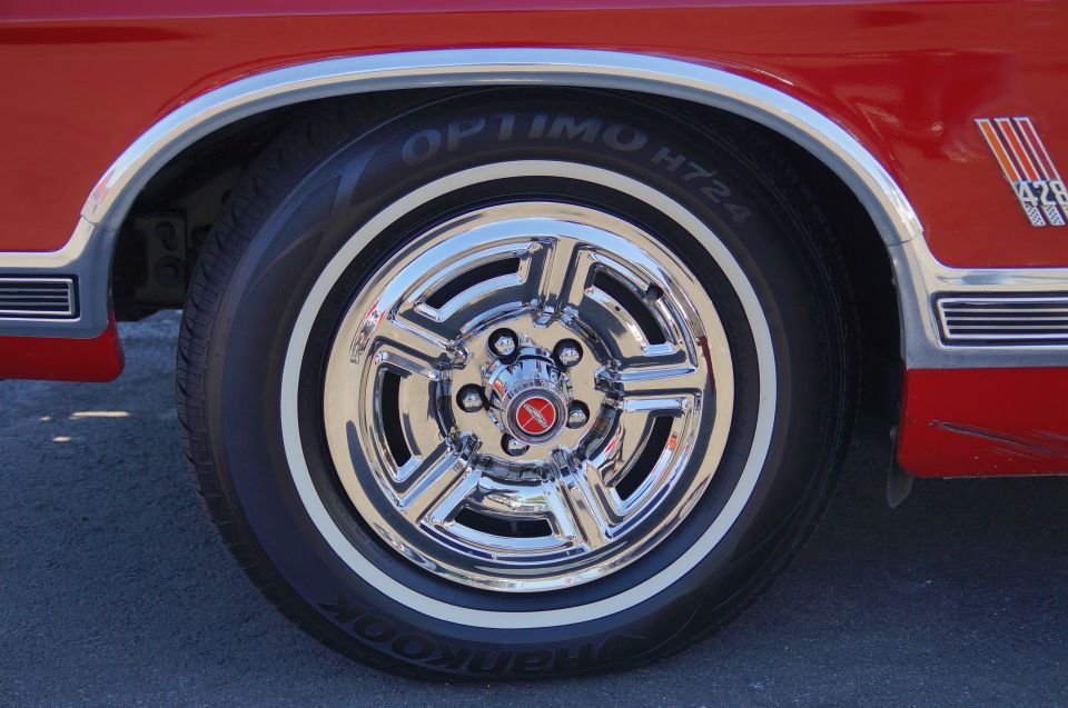 Red car's front passenger-side wheel and fender with chrome rim and "OPTIMO H724" tire.
