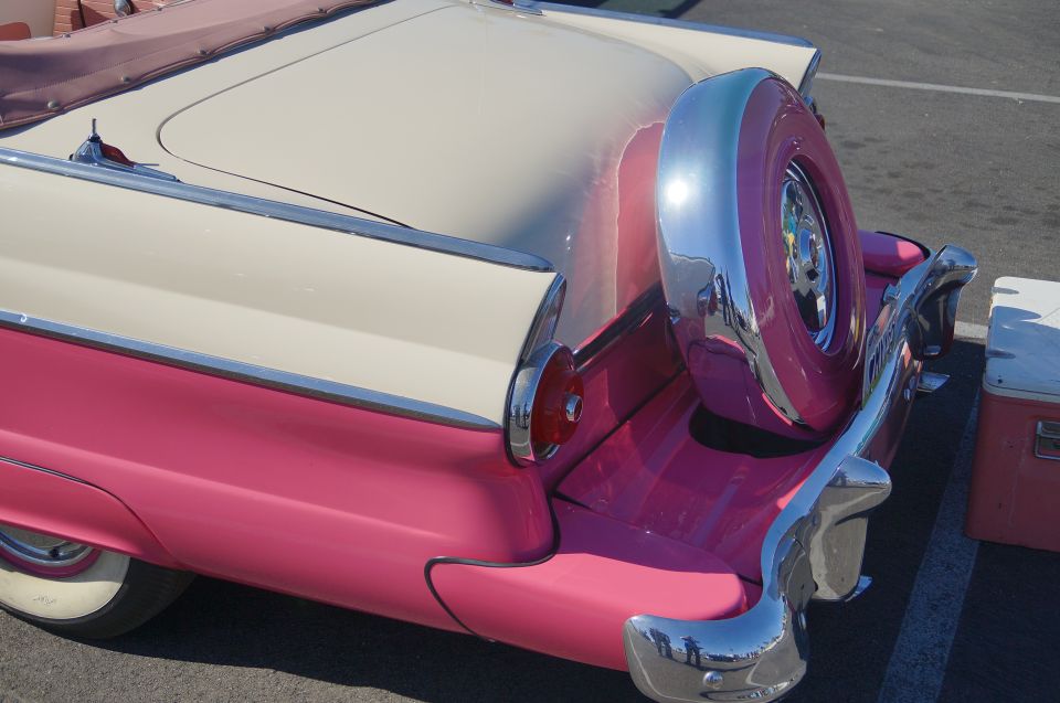 Rear passenger side of a pink and cream vintage convertible with external spare tire.