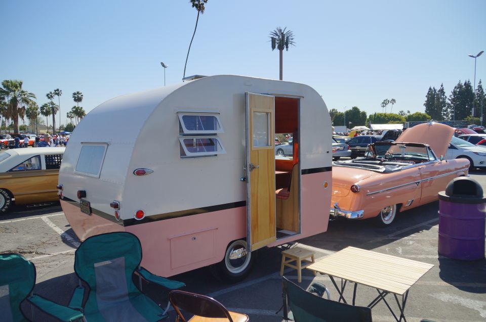 Vintage travel trailer and peach convertible at a car show.