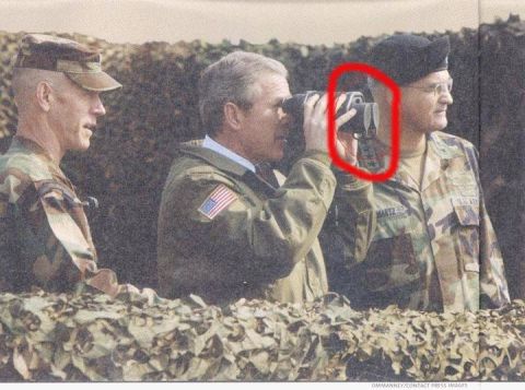 1988 Ford Bronco - Three men in military attire are positioned behind camouflage netting, with one man using binoculars.