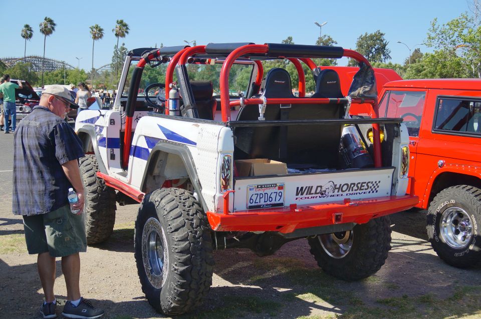 Modified white and blue off-road SUV with red roll cage and large tires, parked next to a red SUV.