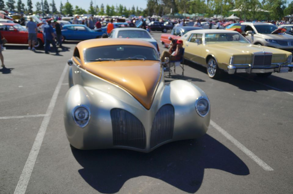 Silver and gold custom hot rod with a large grille parked in a lot.