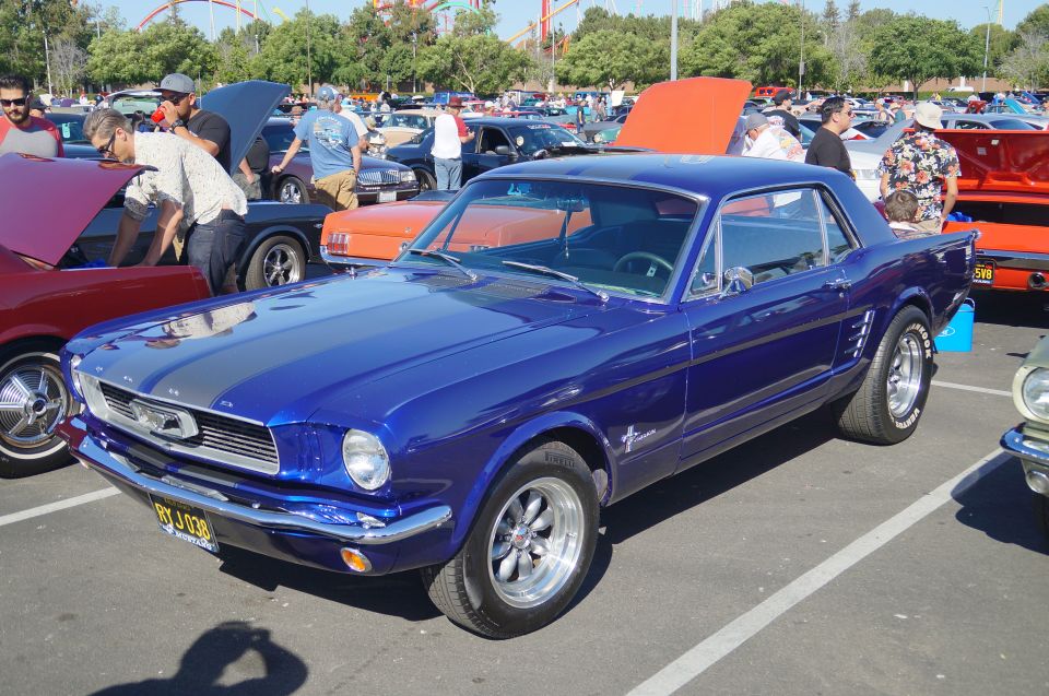 Blue 1960s Ford Mustang coupe with silver stripes, parked at a car show.