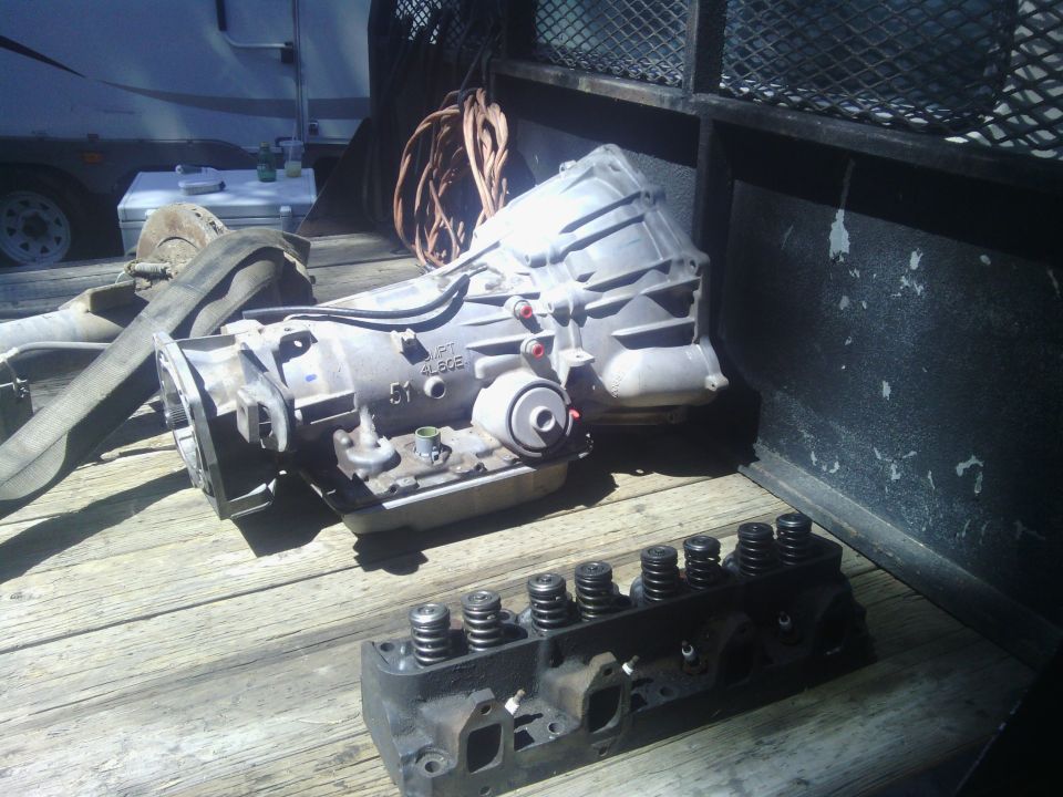 Silver automatic transmission and black cylinder head on a wooden surface.