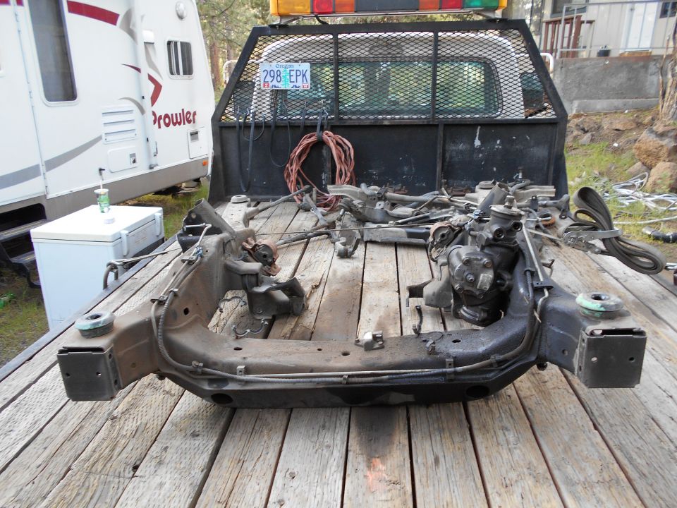 Disassembled front subframe assembly with steering components on a wooden surface.