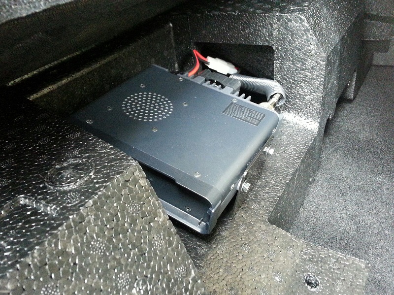 Dark gray radio mounted in foam insert in vehicle trunk.