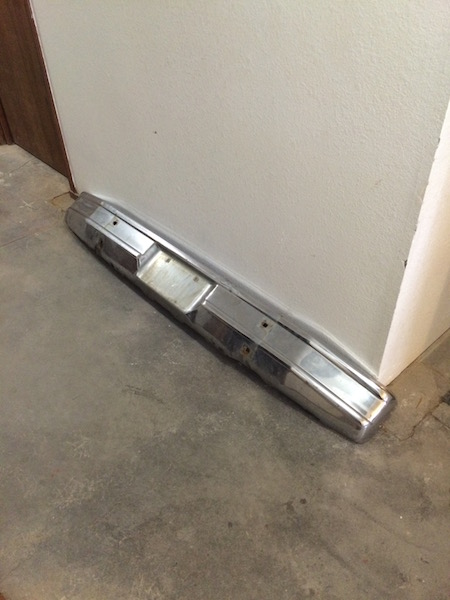 1981 Ford Bronco - A chrome front bumper is leaning against a white wall on a concrete floor. The bumper has several mounting holes and shows some signs of we…