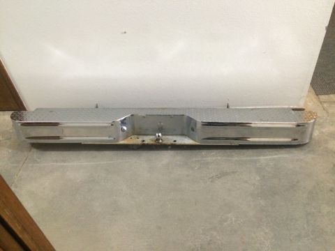 1981 Ford Bronco - A chrome rear bumper with a diamond plate step is shown lying on a concrete floor in front of a white wall. The bumper has a trailer hitch…
