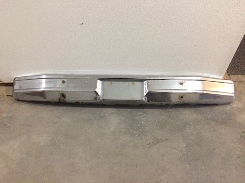 Chrome rear bumper with license plate cutout, mounted on a wall.