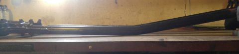 1991 Ford Bronco - A dark-colored, elongated metal part with a bent section is resting on a wooden surface against a yellow wall. The part appears to be a com…