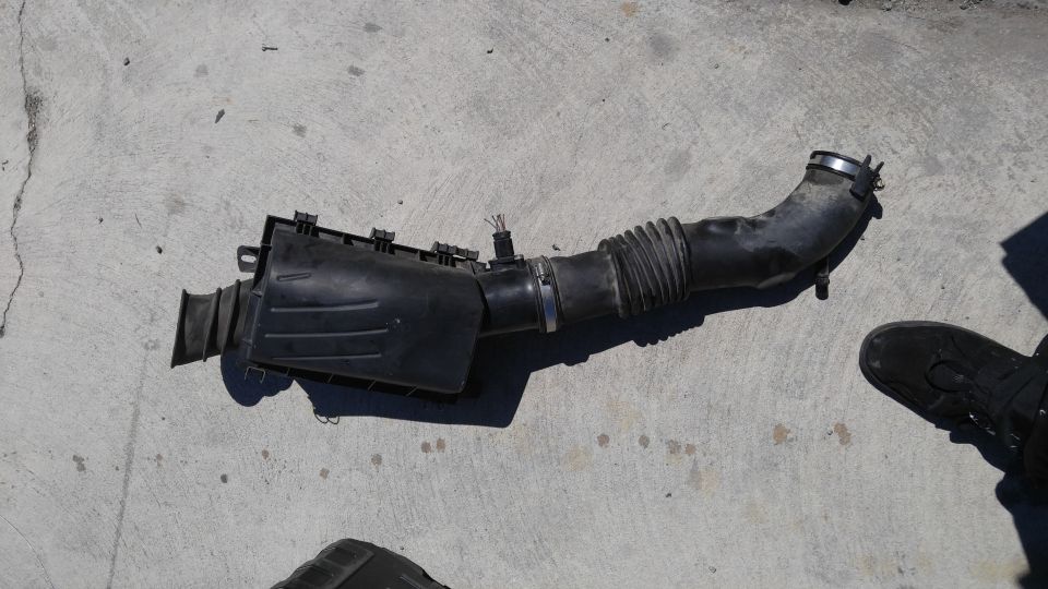 Black plastic air intake assembly with corrugated hose on concrete.