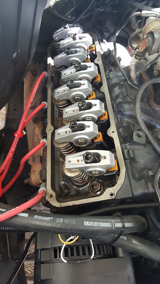 Close-up of Ford V8 engine valve train with rocker arms, springs, and red spark plug wires.