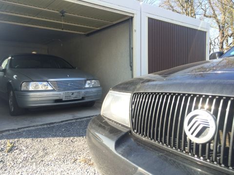 1999 Ford Fairlane - A silver sedan is parked inside a garage, facing forward. A black car is partially visible in the foreground, also facing forward.