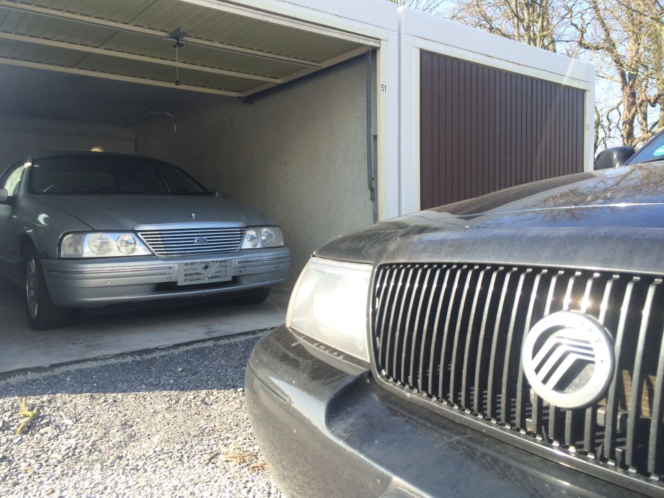 Silver sedan in a garage with a black car in front