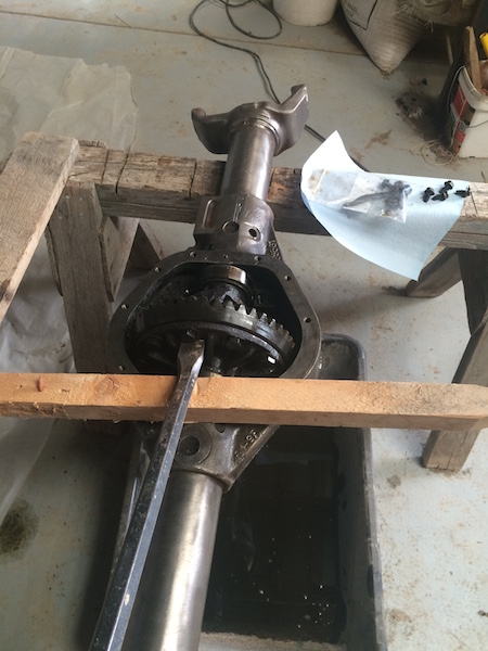 1981 Ford Bronco - A differential assembly is disassembled and supported by wooden blocks. A pry bar is being used to separate components, with a bag of faste…