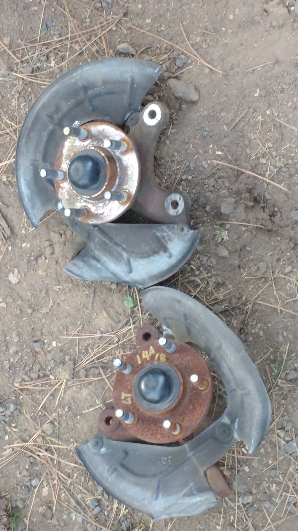 Two automotive wheel hubs with brake dust shields on the ground. One is rusty with markings.