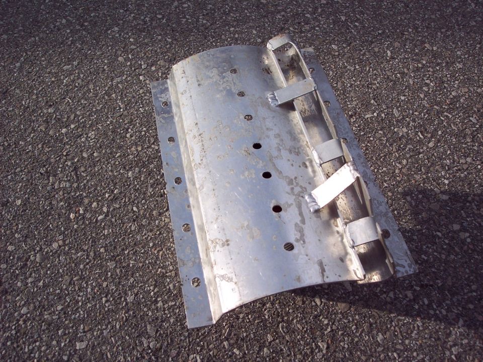 Curved metallic automotive part with holes and brackets on asphalt.