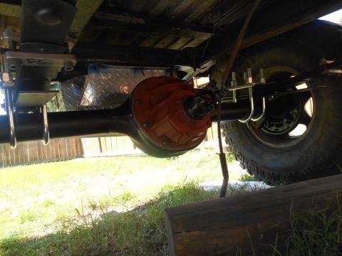1972 Ford Bronco - An underside view of a vehicle's rear axle assembly, featuring a bright orange differential housing and U-bolts securing leaf springs to th…