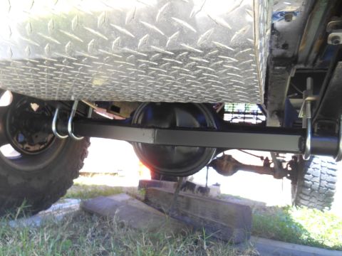 1972 Ford Bronco - The underside of a vehicle shows the rear axle assembly and leaf springs, secured by U-bolts. A diamond plate metal tank is mounted above t…